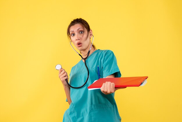 Medico femminile di vista frontale in camicia medica con lo stetoscopio e le note sul colore giallo del virus della salute di covid dell'emozione del medico dell'ospedale della scrivania