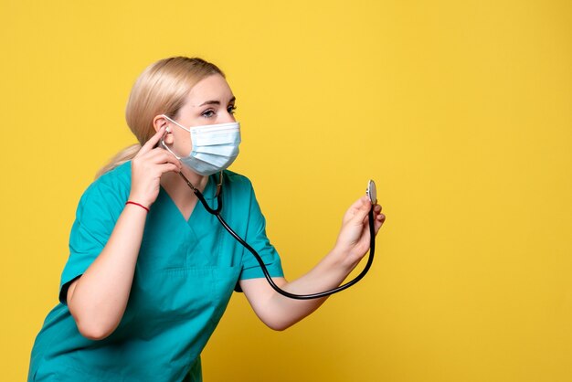 Medico femminile di vista frontale in camicia medica e maschera con lo stetoscopio, pandemia dell'infermiera di salute dell'ospedale del medico covid-19