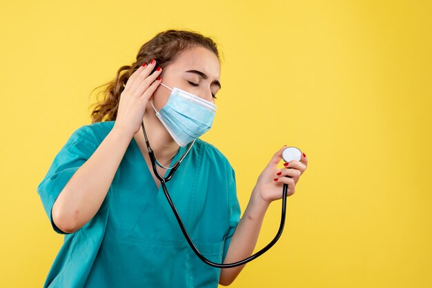 Medico femminile di vista frontale in camicia medica e maschera con lo stetoscopio, salute covid-19 di emozione di colore uniforme del virus