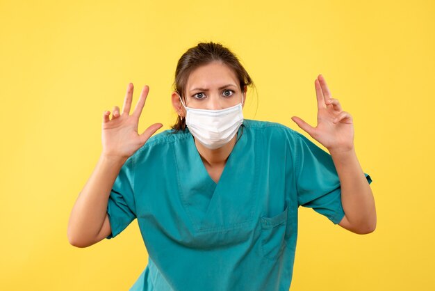 Medico femminile di vista frontale in camicia medica e maschera sterile su fondo giallo
