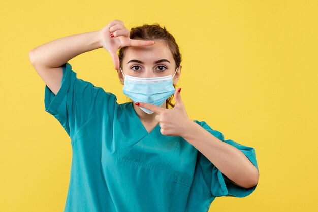 Medico femminile di vista frontale in camicia medica e posa della maschera, uniforme covid-19 pandemica di colore di salute del virus