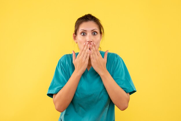 Medico femminile di vista frontale in camicia medica scioccato su priorità bassa gialla