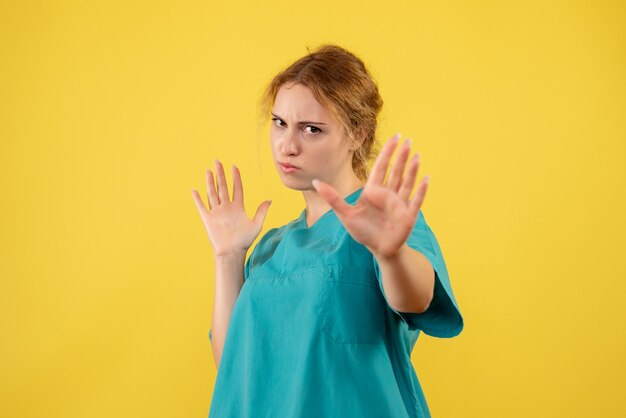 Medico femminile di vista frontale in camicia medica sul colore giallo della medicina di salute dell'infermiera dell'ospedale medico dello scrittorio covid-19