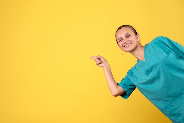 Medico femminile di vista frontale in camicia medica sull'infermiera di emozione di colore dell'ospedale del medico di salute dello scrittorio giallo