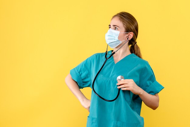 Medico femminile di vista frontale in maschera su covid pandemia di virus di salute di sfondo giallo