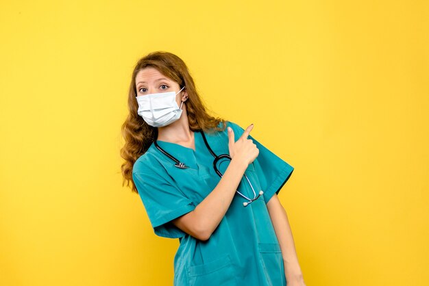 Medico femminile di vista frontale in maschera sullo spazio giallo chiaro