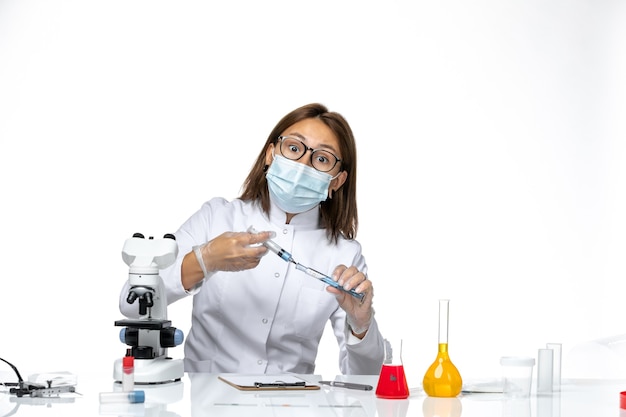 Medico femminile di vista frontale in vestito medico bianco con maschera a causa dell'iniezione della holding covid sullo spazio bianco-chiaro