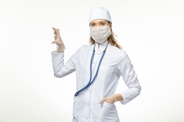 Medico femminile di vista frontale in vestito medico bianco e maschera come protezione dal coronavirus sulla malattia del muro bianco covid- pandemia