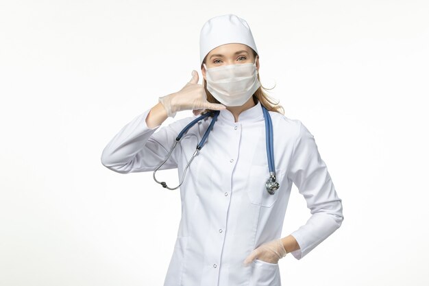 Medico femminile di vista frontale in vestito medico che indossa la maschera a causa del coronavirus sul virus della malattia della parete bianca chiara covid - malattia della malattia pandemica