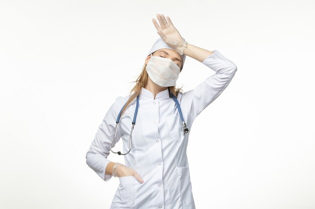 Medico femminile di vista frontale in vestito medico con maschera e guanti a causa del coronavirus sulla malattia del muro bianco chiaro malattia pandemica covid- virus