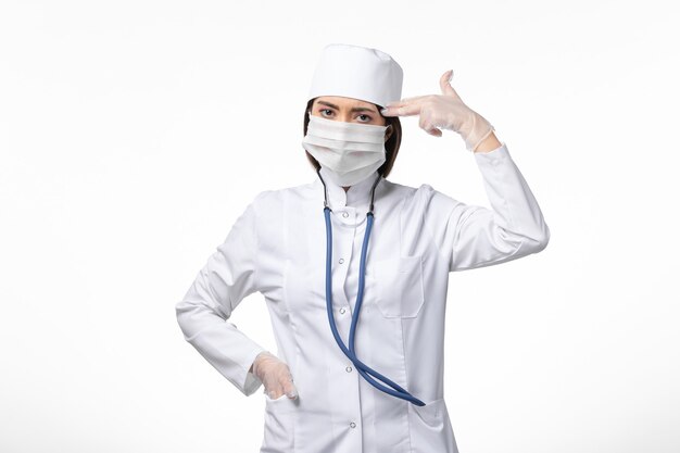 Medico femminile di vista frontale in vestito medico sterile bianco con maschera a causa del coronavirus sulla malattia del muro bianco covid-virus pandemico