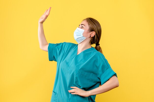 Medico femminile di vista frontale nella mascherina sterile sulla salute covid del virus pandemico dello scrittorio giallo