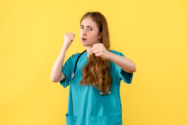 Medico femminile di vista frontale nella posa del combattente sull'emozione di salute dell'ospedale del medico del fondo giallo