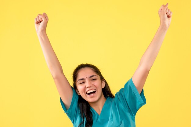 Medico femminile felice di vista frontale in uniforme che mostra la sua felicità su fondo isolato giallo