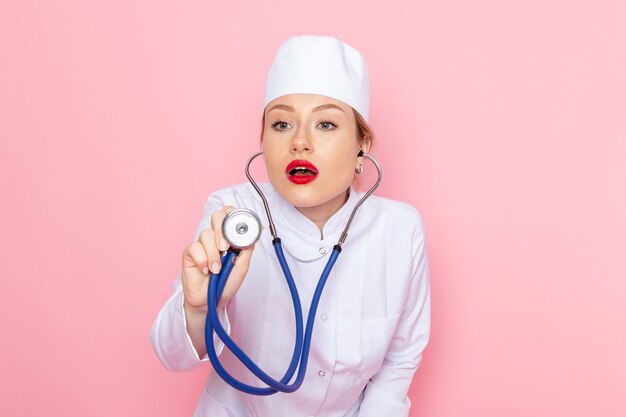 Medico femminile giovane di vista frontale in vestito bianco con lo stetoscopio blu che misura sullo spazio rosa femminile