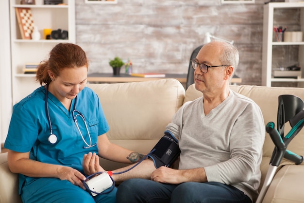 Medico femminile in casa di cura che controlla la pressione sanguigna dell'uomo anziano.