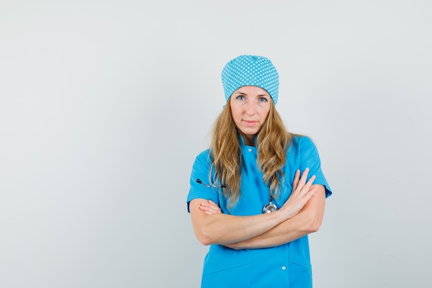 Medico femminile in piedi con le braccia incrociate in uniforme blu e guardando fiducioso
