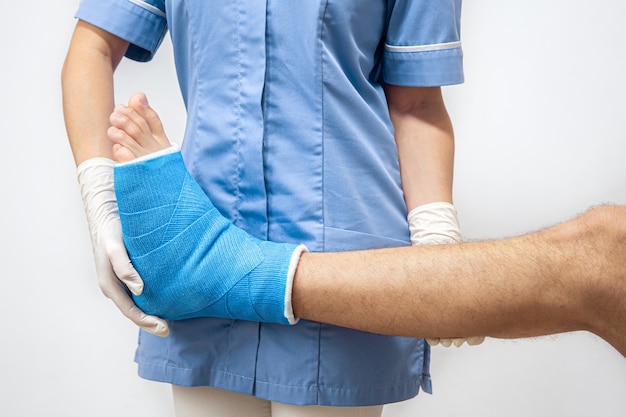 Medico femminile in un abito medico blu che controlla la gamba rotta sul paziente maschio.