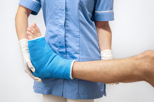 Medico femminile in un abito medico blu che controlla la gamba rotta sul paziente maschio.