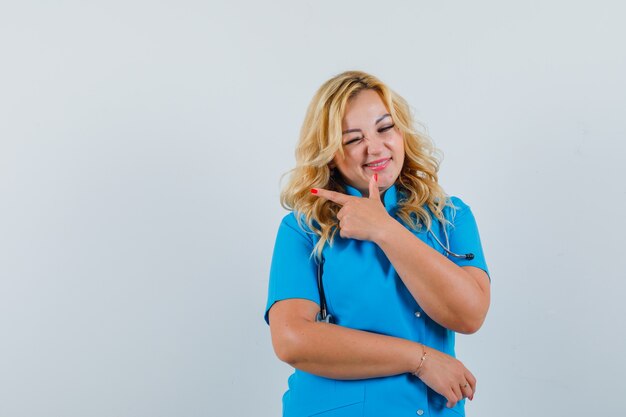 Medico femminile in uniforme blu che indica da parte mentre fa l'occhiolino allo spazio per il testo