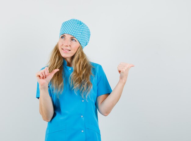 Medico femminile in uniforme blu che indica i pollici in su al lato e che sembra allegro