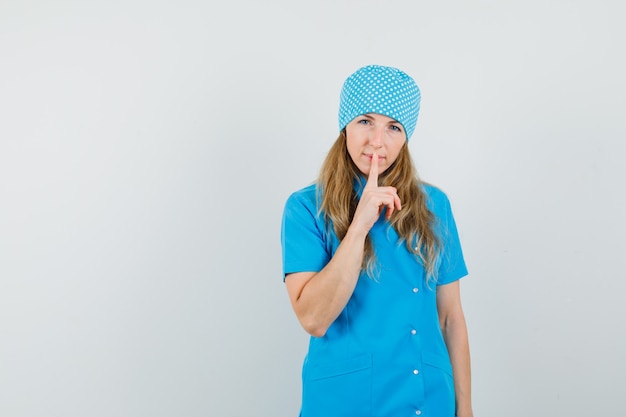 Medico femminile in uniforme blu che mostra gesto di silenzio e che osserva attento