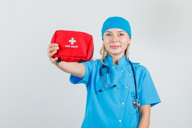 Medico femminile in uniforme blu che mostra il kit di pronto soccorso e sembra allegro