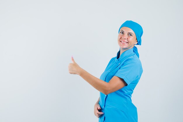 Medico femminile in uniforme blu che mostra pollice in su e che sembra gioioso, vista frontale.