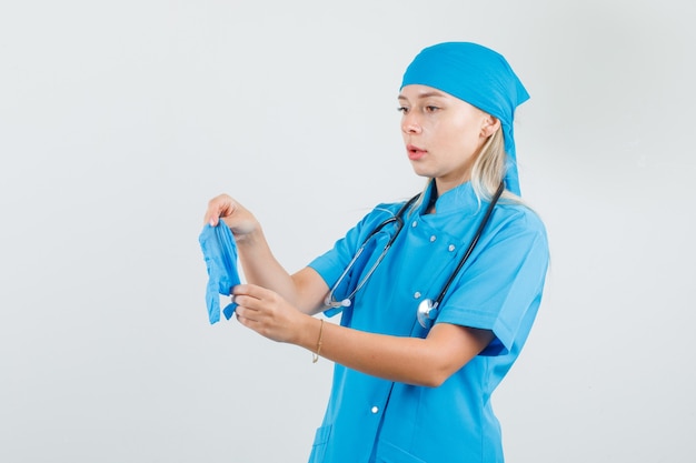 Medico femminile in uniforme blu che tiene i guanti medici e che osserva attento