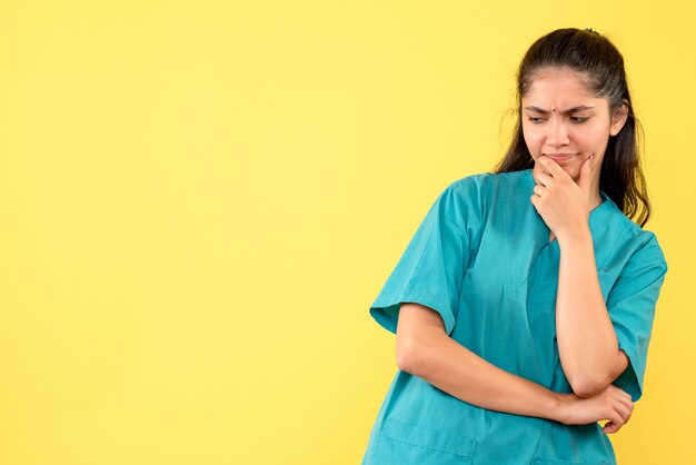 Medico femminile premuroso vista frontale in uniforme in piedi su sfondo giallo isolato