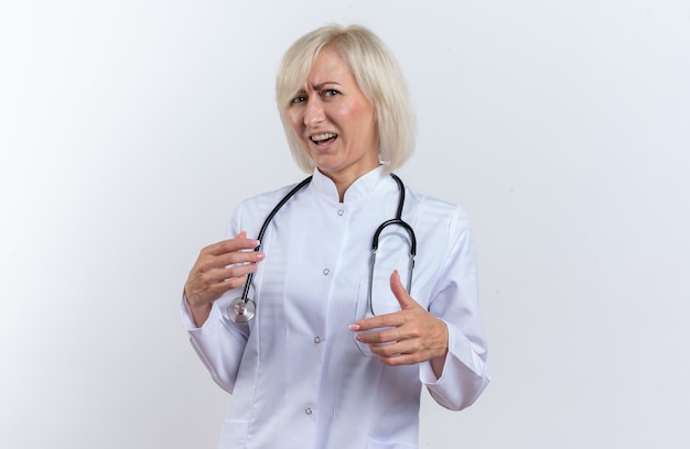 Medico femminile slava adulto scontento in abito medico con stetoscopio che guarda la macchina fotografica isolata su fondo bianco con lo spazio della copia