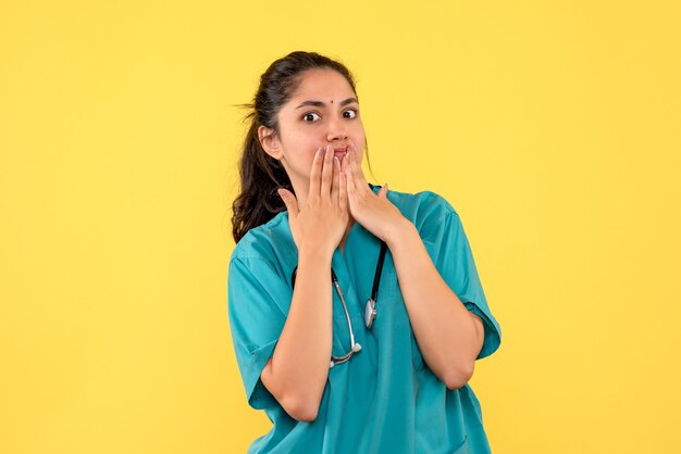 Medico femminile sorpreso vista frontale con stetoscopio in piedi su sfondo giallo