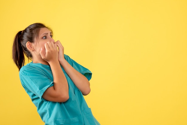 Medico femminile vista frontale in camicia medica con espressione spaventata su sfondo giallo