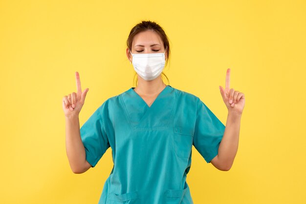 Medico femminile vista frontale in camicia medica e con maschera sterile su sfondo giallo
