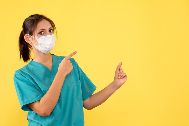 Medico femminile vista frontale in camicia medica e con maschera sterile su sfondo giallo