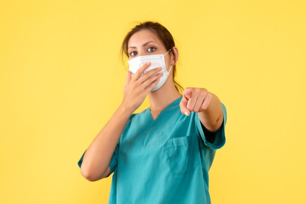 Medico femminile vista frontale in camicia medica e con maschera sterile su sfondo giallo