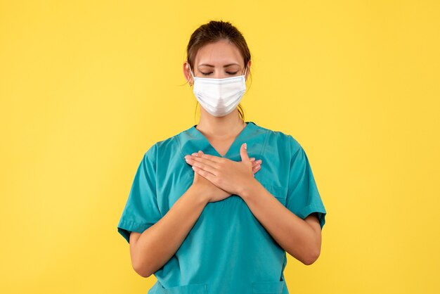 Medico femminile vista frontale in camicia medica e maschera su sfondo giallo