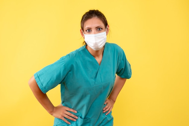 Medico femminile vista frontale in camicia medica e maschera su sfondo giallo