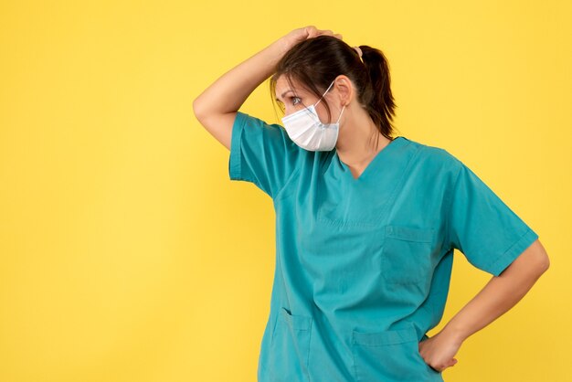 Medico femminile vista frontale in camicia medica e maschera su sfondo giallo