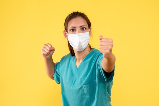 Medico femminile vista frontale in camicia medica e maschera su sfondo giallo