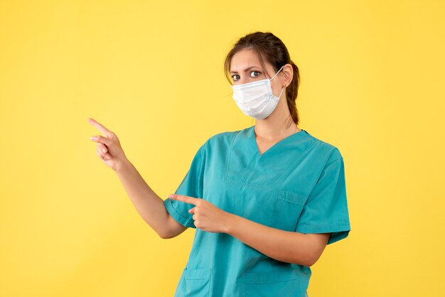 Medico femminile vista frontale in camicia medica e maschera su sfondo giallo