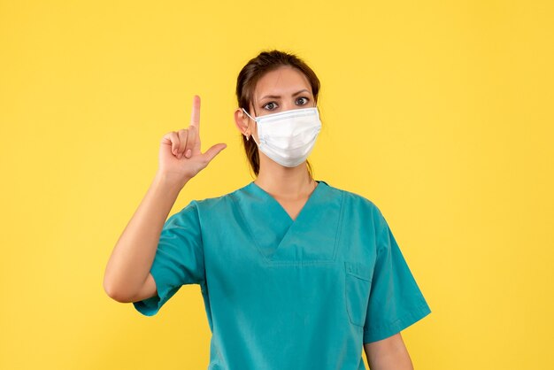 Medico femminile vista frontale in camicia medica e maschera su sfondo giallo