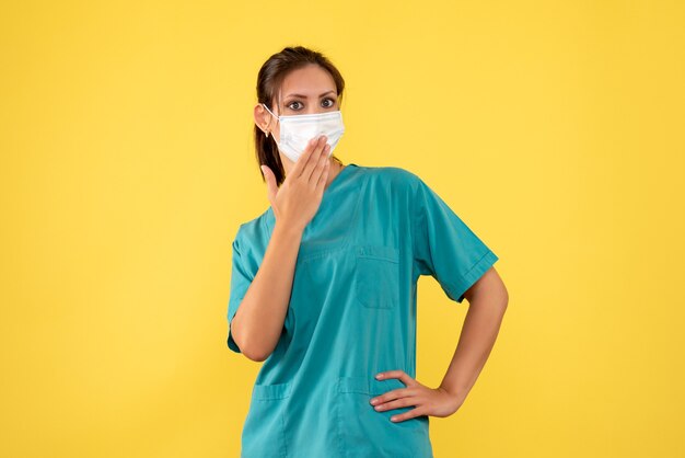 Medico femminile vista frontale in camicia medica e maschera su sfondo giallo