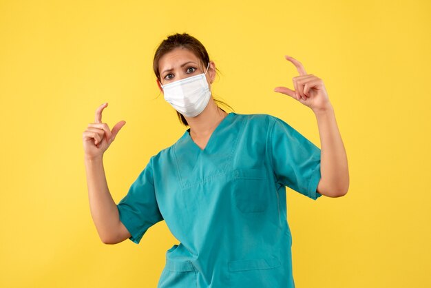 Medico femminile vista frontale in camicia medica e maschera su sfondo giallo