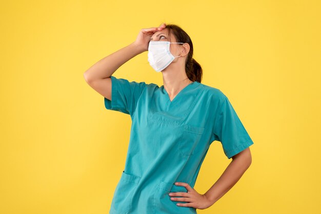 Medico femminile vista frontale in camicia medica e maschera su sfondo giallo