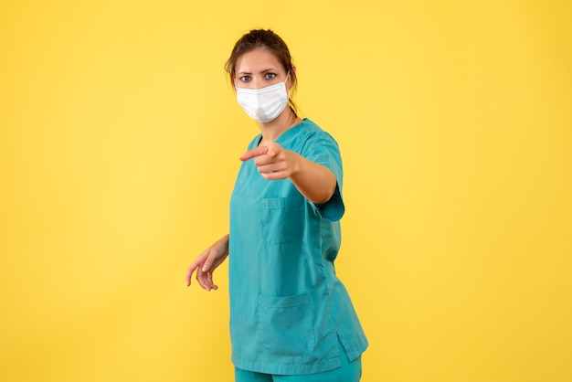Medico femminile vista frontale in camicia medica e maschera su sfondo giallo