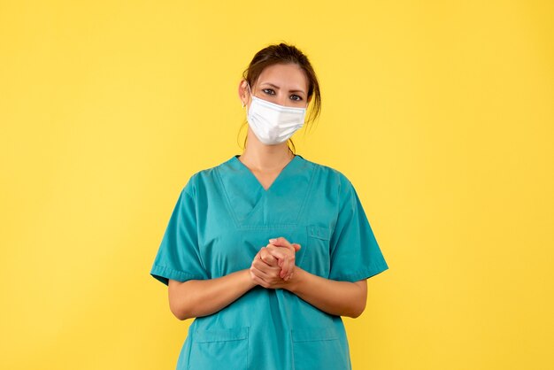 Medico femminile vista frontale in camicia medica e maschera su sfondo giallo