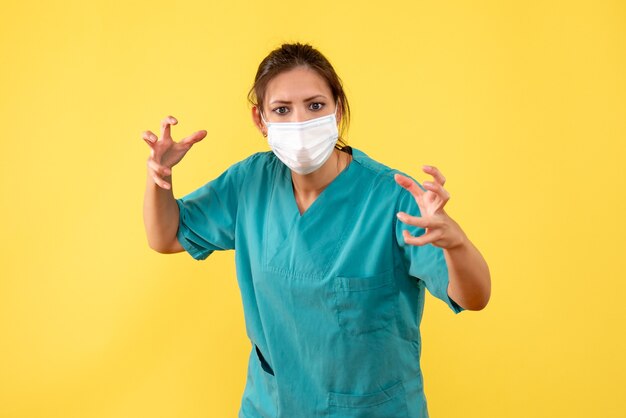 Medico femminile vista frontale in camicia medica e maschera su sfondo giallo