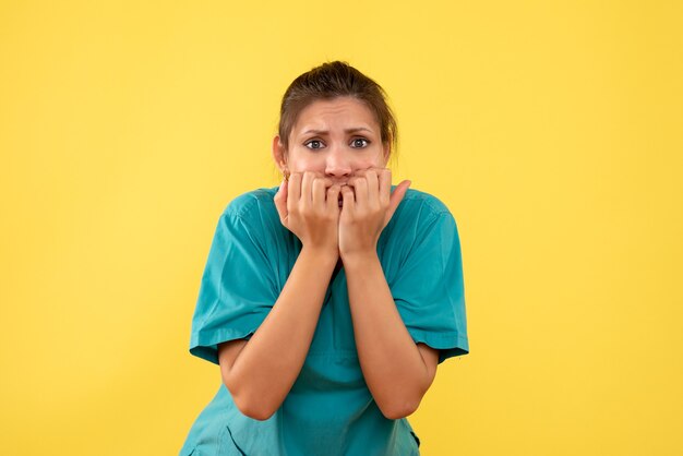 Medico femminile vista frontale in camicia medica spaventato e nervoso su uno sfondo giallo