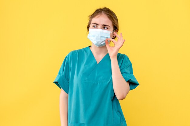 Medico femminile vista frontale in maschera sterile su sfondo giallo salute ospedale covid-pandemia